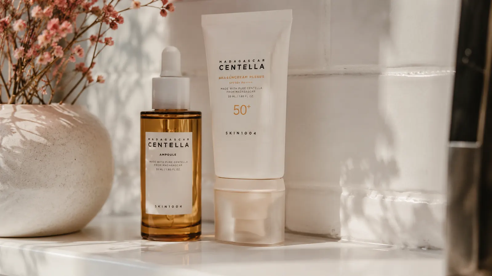 Sunscreen bottle and vitamin C serum side by side on a bathroom countertop, representing morning routine pairing