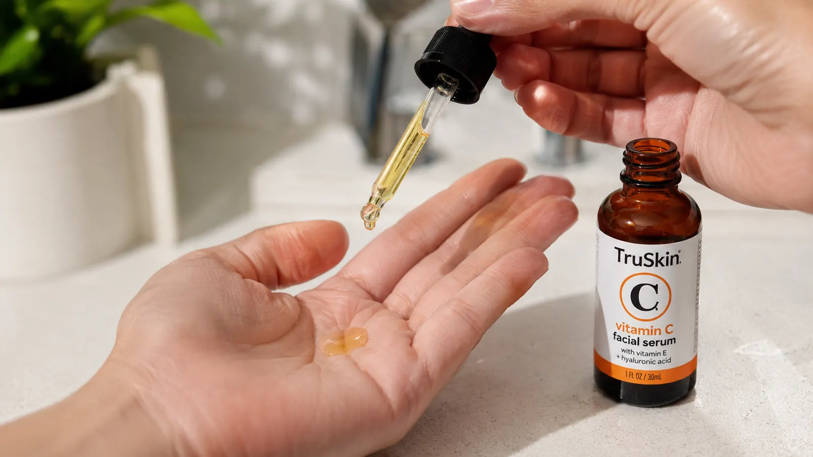 Hand holding TruSkin Vitamin C Serum dropper above palm with a few drops of amber serum