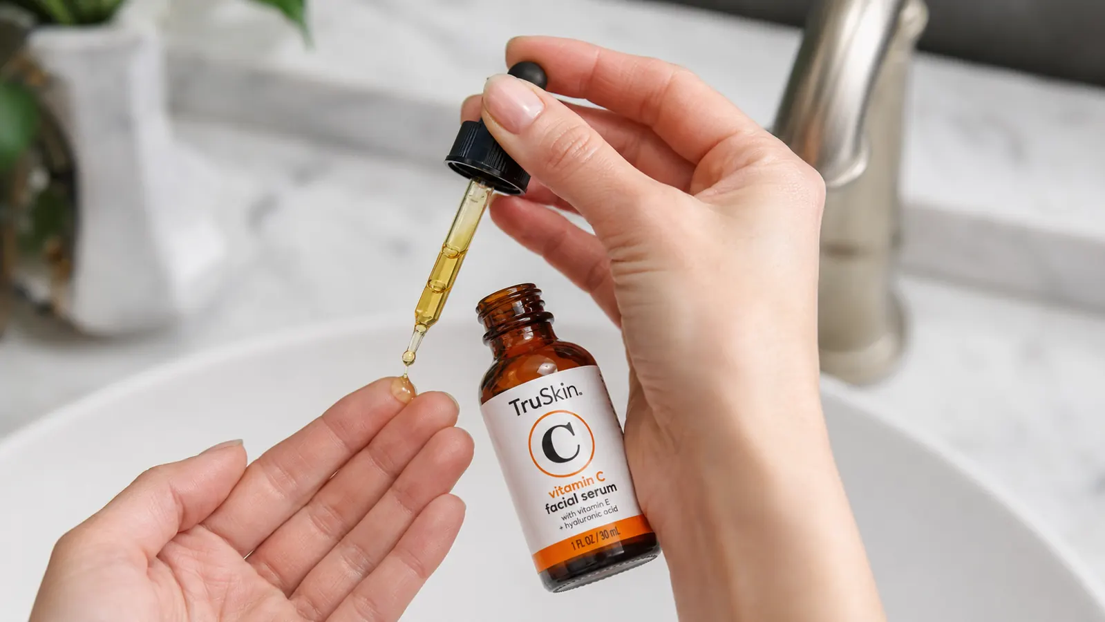 Hand holding the TruSkin Vitamin C Serum bottle, dispensing a few drops onto fingertips